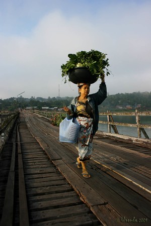 Mon woman with basket of vegetables on her head walking on a wooden Bridge