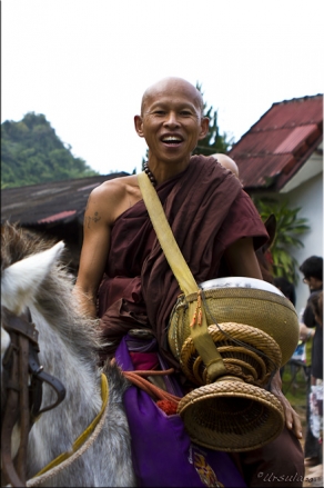 Smiling monk astride a white horse, with a large gold begging bowl.