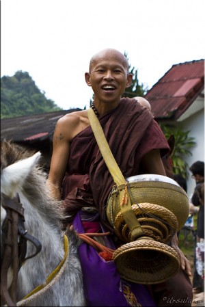 Smiling monk astride a white horse, with a large gold begging bowl.