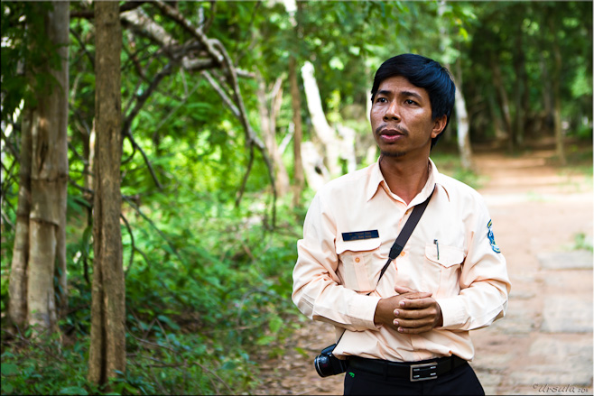 Portrait: Serious-looking Khmer man in long-sleeved shirt in front of jungle.