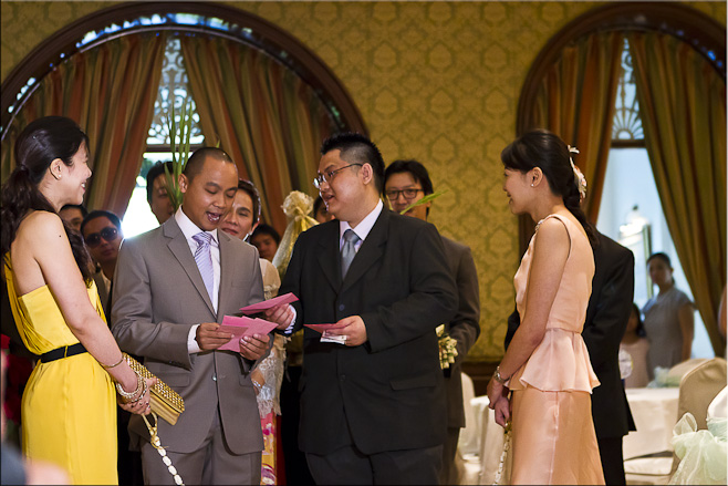 Two young Thai women hold an rope made of flowers, as two Thai men negotiate red envelopes.