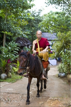 Monk in glasses with his alms bowl, riding a brown horse.