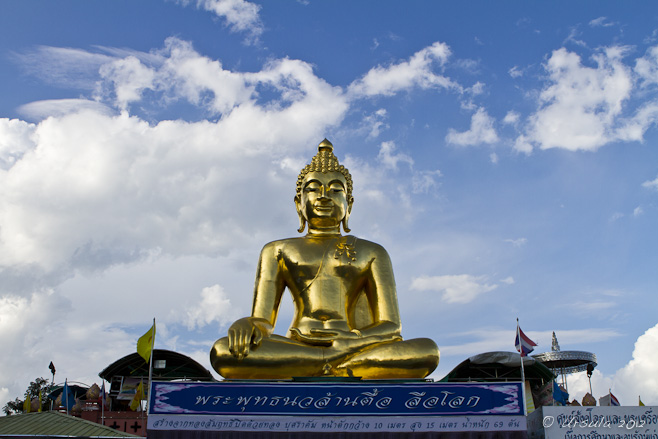 Seated Golden Buddha against a blue sky with white clouds.