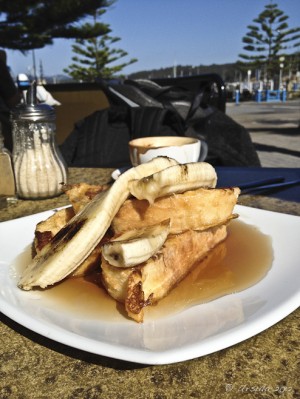 Piled thick French toast with syrup and banana on an outdoor table.