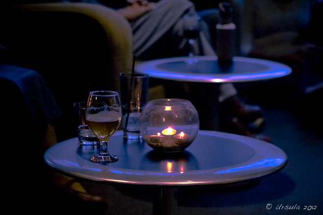 Tea-light candles and drinks on a low table in the dark.