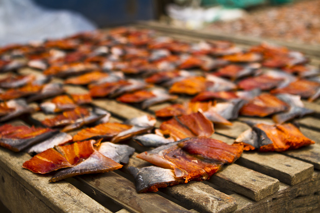 Chunks of red fish lying in the sunshine on wooden slats.