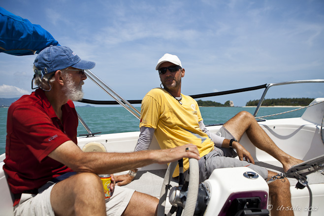 Two men at the helm of a small sailboat.