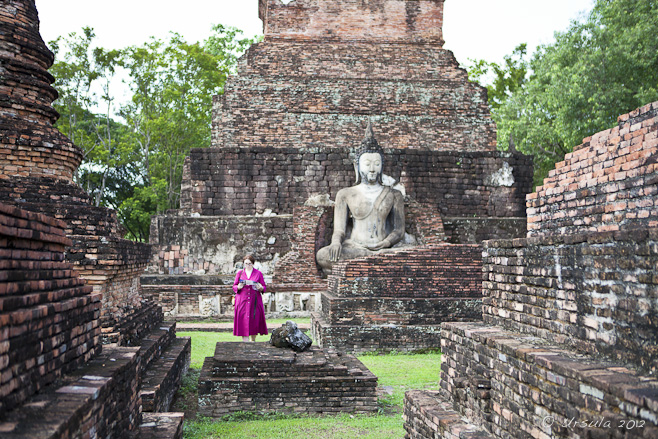 A woman in a hot pink dress among the red-laterite ruins of Sukhothai.