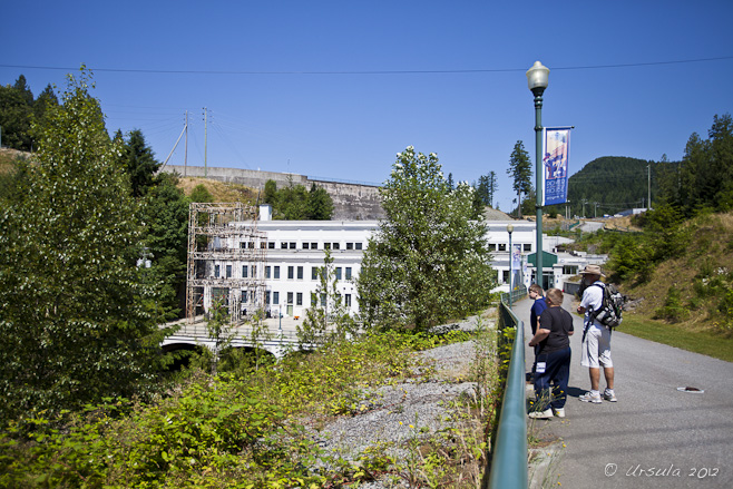 White exterior of the Stave Falls Powerhouse building, set in green trees and bushes.