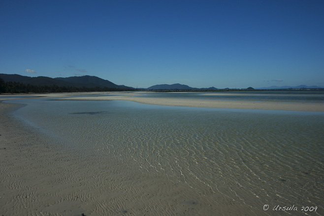 Expanse of rippled sandy beach with a thin layer of water across it.