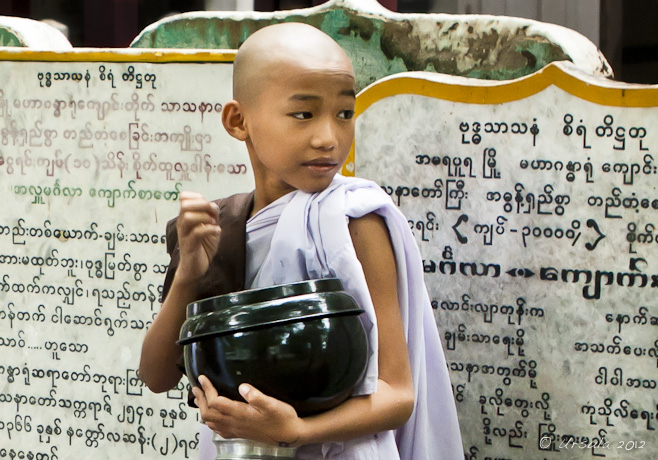 Young novice nun in White, clutching her alms bowl, looking over her shoulder. Mahagandayon Monastery, Mandalay