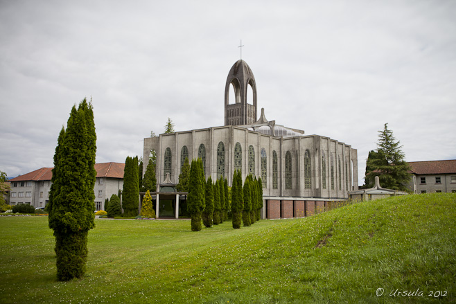 View of Westminster Abbey, Mission, BC from across wet green lawns; gray skies behind.