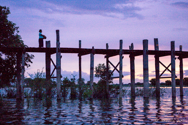 Evening scene on U-Bein Bridge: a woman with a basket stands on the wooden bridge, silhouetted against a purple sky, Amarapura, Myanmar