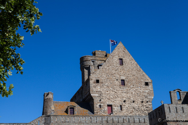 Medieval buildings over a city wall, against a blue sky, flying a French flag. Saint-Malo, Bretagne