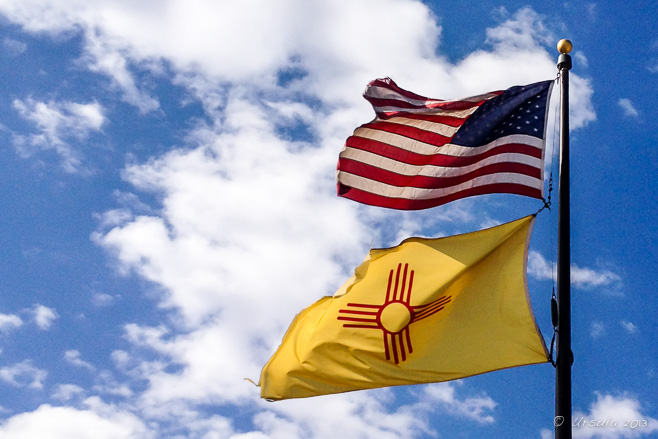Flying American and New Mexican Flags against a blue sky with high white clouds.