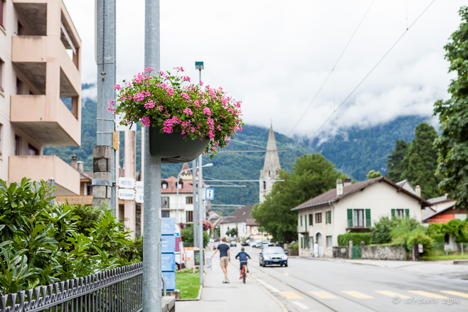 Flower pot on a light pole; Central Street in Bex, Switzerland, in the background.