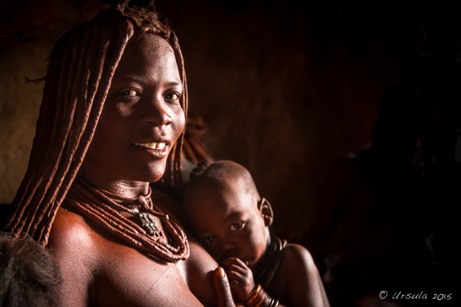 Portrait: Himba woman in a dark hut nursing her child, Otjomazeva Namibia