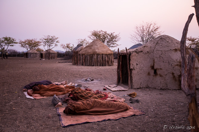 People in bed rolls in front of Himba huts, Otjomazeva Village Namibia