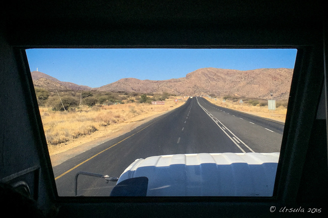 View through a truck front window over an empty Namibian roadway.