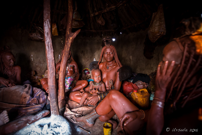 Himba women and a child inside a dark hut, Kunene Region, Namibia