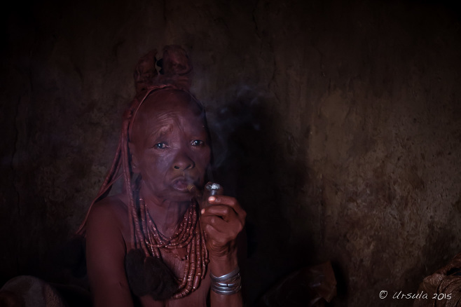 Old Himba woman smoking a pipe in a dark hut, Kunene, Namibia