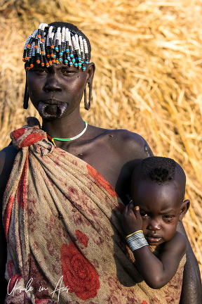 Mursi woman with beaded hair and a baby on her hip, Ethiopia