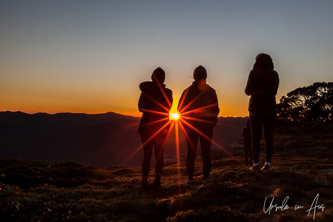 Sunburst through three people silhouetted at sunrise, Thredbo, NSW Australia