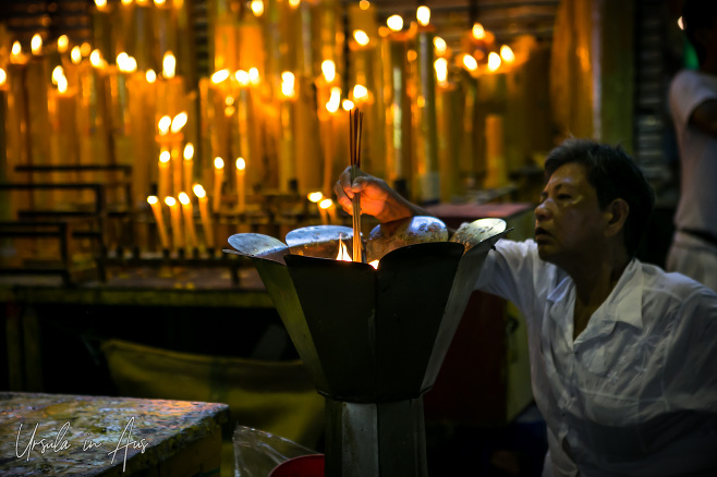 A woman lighting incense in the light of giant candles, Chinatown Bangkok