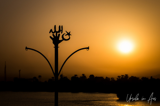 A hamsa symbol with a star and crescent and the word "Allah" in Arabic against a sunset sky, the Nile, Luxor Egypt.