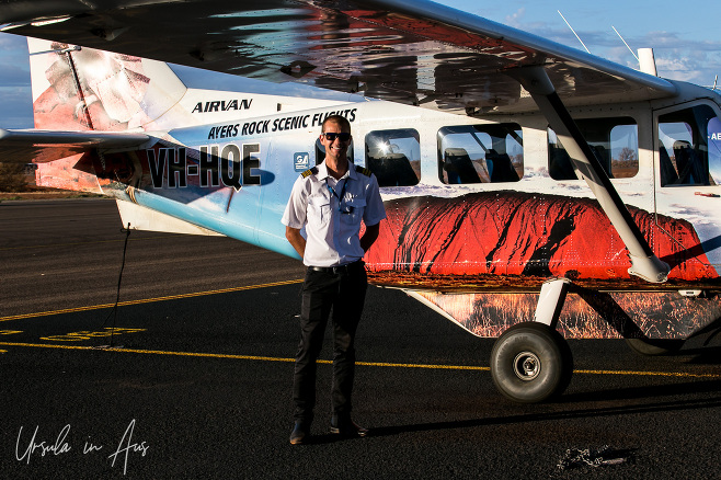 Young pilot standing outside a brightly decorated Ayers Rock Scenic Flight airplane, NT Australia