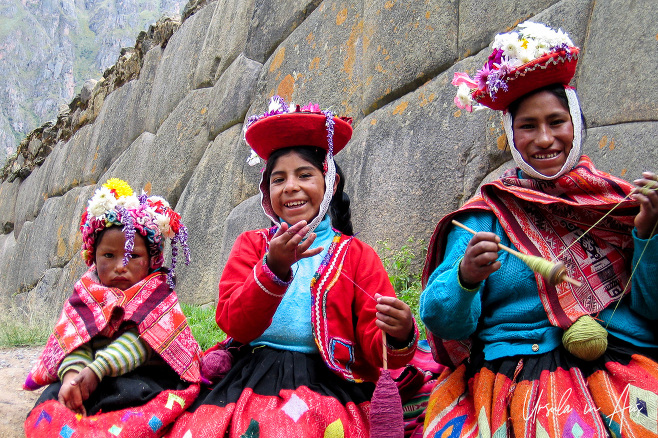 A woman a girl and a toddler in traditional Quechua clothing spinning wool, Ollantaytambo Peru