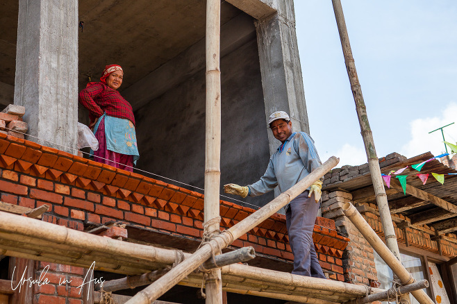 Newari man and woman bricklaying on an upper story of a Bungamati house, Nepal