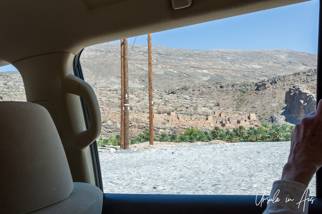 Clay brick buildings and a dry mountainside from inside a car, Hajar Mountains Oman