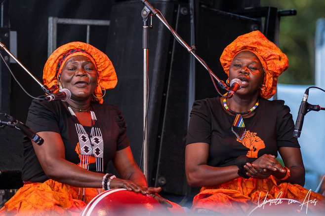 Two seated women from Les Aunties, in black and orange, on stage singing, Vancouver Island Musicfest, Comox BC Canada